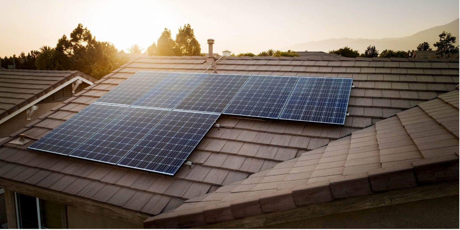 Golden-hour view of a residential rooftop solar array with mountains in the distance